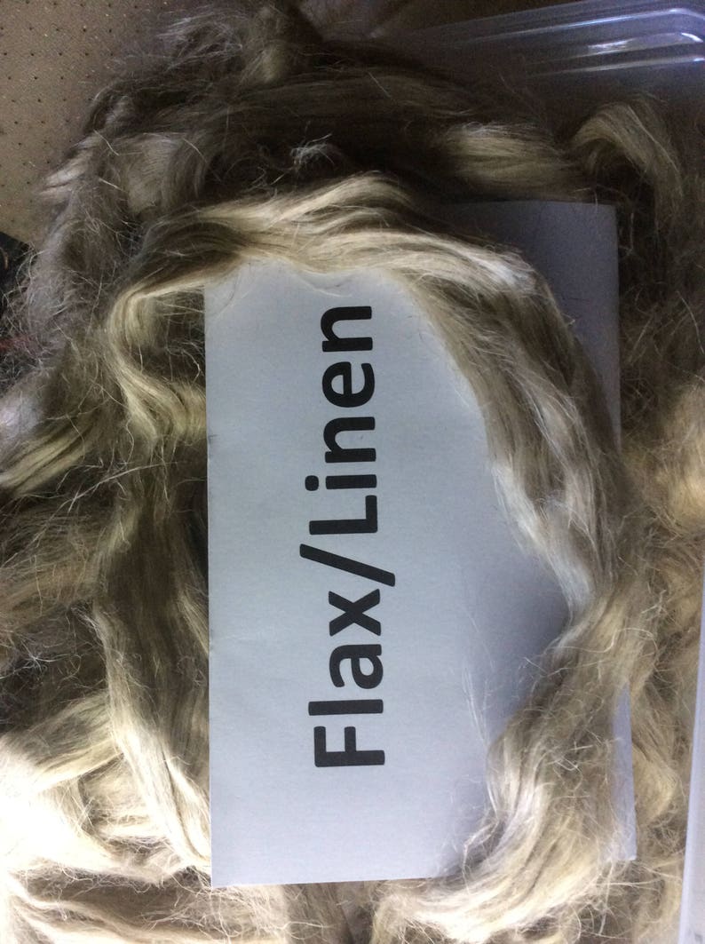 May include: A close-up of a pile of light brown flax fibers. A white label with the text "Flax/Linen" is visible.