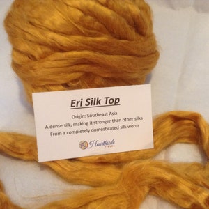 May include: A close-up of a golden yellow Eri silk top, a type of silk known for its strength and durability. The silk is from a domesticated silk worm and is from Southeast Asia. The text on the card reads "Eri Silk Top", "Origin: Southeast Asia", "A dense silk, making it stronger than other silks", "From a completely domesticated silk worm", and "Hearthside Fibers".