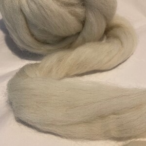 May include: A large ball of light gray wool roving. The roving is soft and fluffy, and it is perfect for felting, spinning, or other fiber crafts.
