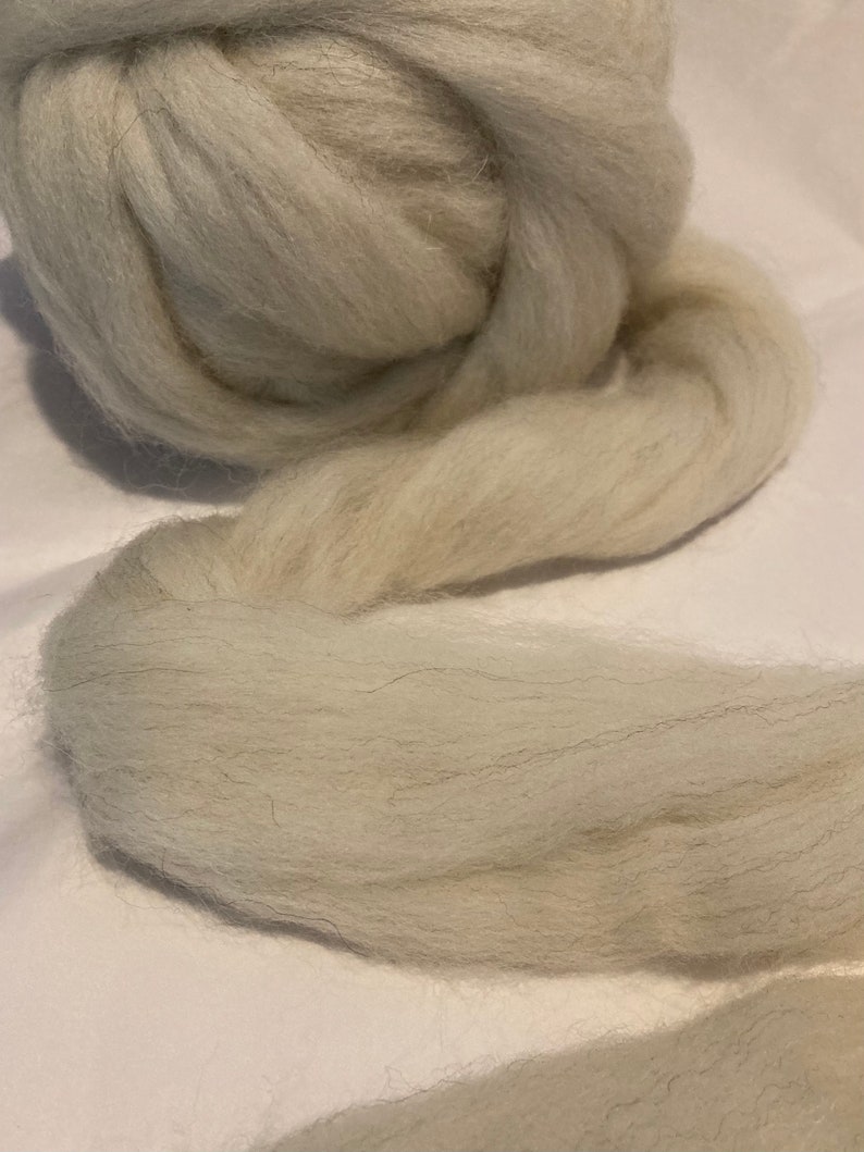 May include: A large ball of light gray wool roving. The roving is soft and fluffy, and it is perfect for felting, spinning, or other fiber crafts.