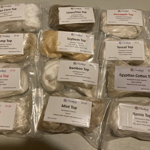 May include: A collection of 10 small plastic bags, each containing a different type of natural fiber, labeled with the fiber type and price. The fibers include Ingeo Corn Top, Hemp Top, Banana Top, Rose Top, Linen/Flax Top, Soybean Top, Bamboo Top, Tencel Top, Egyptian Cotton Top, and Ramie Top.