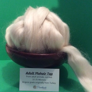 May include: A white mohair top, a type of wool fiber, is displayed in a brown bowl. The top is from adult angora goats and measures 32-35 microns. The label reads "Adult Mohair Top, From adult animals, not kids, 32-35 Microns, Angora goats originally from Turkey, Hearthside Fibers."