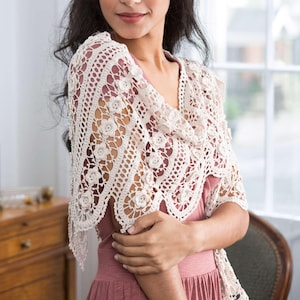 Op de afbeelding: Crèmekleurige, open geweven gehaakte sjaal met bloemaccenten. De sjaal heeft een delicaat, kantachtig ontwerp met herhaalde bloemmotieven. Het kledingstuk is over de schouders gedrapeerd en toont het ingewikkelde vakmanschap en de textuur van het handgemaakte stuk.