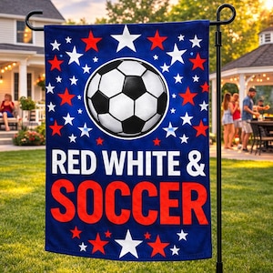 May include: A blue garden flag with a soccer ball design, red and white stars, and the words "RED WHITE & SOCCER". The flag is displayed on a black metal stand in a front yard with a house and people in the background.