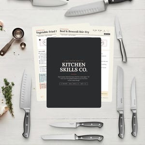 May include: A collection of kitchen knives surrounding a black book cover with the text Kitchen Skills Co. and recipe pages titled Vegetable Fried Rice and Beef & Broccoli Stir-Fry. The text reads Kittchen Skills Co. 24 Recipes. Ages 7-15.