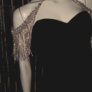 Peut inclure: Un ensemble d'épaule et de cou argenté étincelant avec des franges pendantes. Les bijoux sont présentés sur un mannequin portant une robe noire. Les franges descendent le long des bras, créant un look glamour.