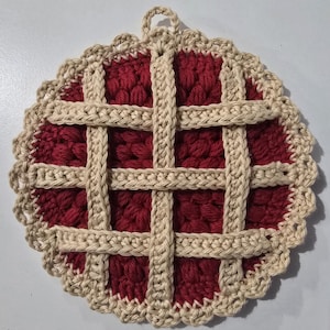 May include: A handmade, round crochet potholder resembling a pie. The center is a deep red, with a lattice crust design in a light tan color. The edge is scalloped, and a loop is attached for hanging.