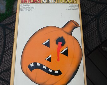 May include: A hardcover book titled Tricks and Treats, edited by Joe Gores and Bill Pronzini. The cover features a large orange jack-o'-lantern with black triangular eyes, a black mouth, and a black bullet hole with red blood dripping down.
