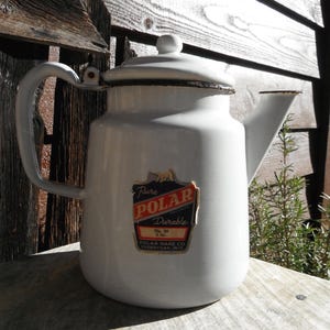 May include: White enamelware Polar brand coffee pot with a black rim and handle. The pot has a lid with a small knob and a spout. A label on the front reads "Pure Polar Durable" and "Polar Ware Co. Sheboygan, Wis."
