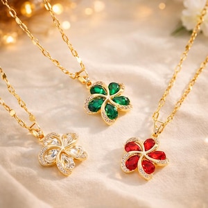 Peut inclure: Trois colliers dorés avec des pendentifs en forme de fleurs. Un pendentif est orné de cristaux transparents, un autre de cristaux verts et le troisième de cristaux rouges. Chaque fleur est bordée de petits cristaux transparents.