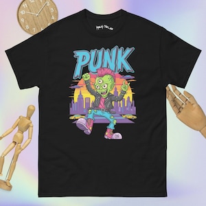 Puede incluir: Camiseta negra con un diseño gráfico colorido de un personaje de piel verde con tres ojos, con una chaqueta de cuero y vaqueros. La palabra "PUNK" está en letras azules sobre el personaje. La camiseta tiene cuello redondo.