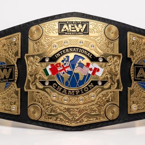 Puede incluir: Un cinturón de lucha libre AEW International Championship chapado en oro con una correa de cuero negro, grabados metálicos intrincados y un emblema central de globo terráqueo con varias banderas nacionales y el texto All Elite Wrestling.