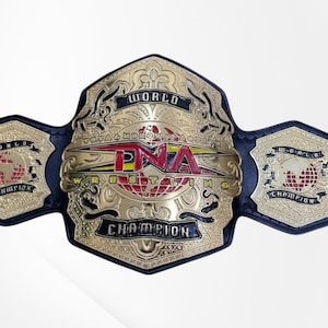 May include: A TNA World Wrestling Champion belt featuring a large, ornate gold-colored central plate with red and black lettering, a globe graphic, and smaller gold side plates attached to a black leather strap with intricate embossed detailing.