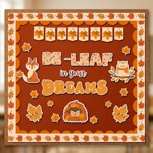 May include: A square cork bulletin board with a decorative border of orange autumn leaves. The center features the text BE-LEAF in your DREAMS, surrounded by cutouts of a fox, an owl, a hedgehog, and various leaves, plus a banner of leaf flags.