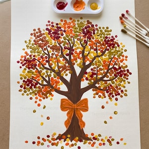 May include: A painting of a tree with a brown trunk and an orange bow tied around it. The leaves are created with dots of paint in shades of red, orange, yellow, and green. A white paint palette with three colors and several cotton swabs are visible.