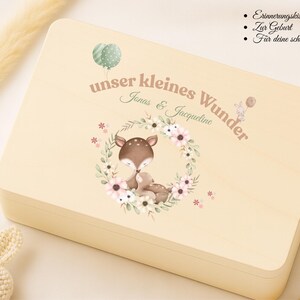 May include: A light-colored wooden keepsake box with a watercolor illustration of a deer and baby deer inside a floral wreath. The box has the text "unser kleines Wunder" and the names "Jonas & Jacqueline".
