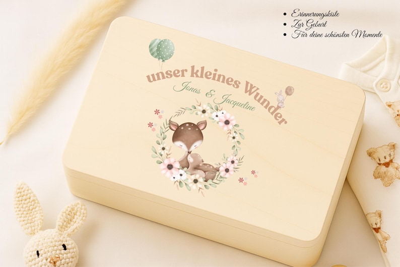 May include: A light-colored wooden keepsake box with a watercolor illustration of a deer and baby deer inside a floral wreath. The box has the text "unser kleines Wunder" and the names "Jonas & Jacqueline".