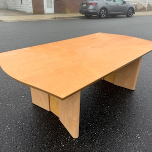 May include: A light-colored wooden table with a unique, curved edge design. The table has a rectangular top and two supporting bases. The table is approximately 72 inches long and 36 inches wide.