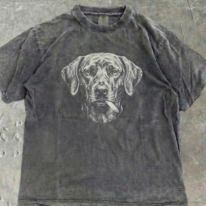 Può includere: Una t-shirt a maniche corte color grigio antracite con una finitura lavata all'acido in stile vintage. Al centro del petto è presente un'illustrazione dettagliata a linee bianche del muso di un cane con una sigaretta tra le labbra.