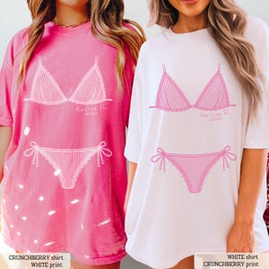 K&ouml;nnte beinhalten: Ein rosafarbenes T-Shirt mit einer wei&szlig;en Bikini-Grafik und dem Text Key West FL est 2026 sowie ein wei&szlig;es T-Shirt mit einer rosafarbenen Bikini-Grafik und dem Text Key West FL est 2026. Beide T-Shirts haben kurze &Auml;rmel und einen Rundhalsausschnitt.