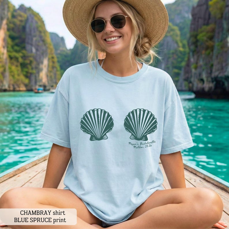 Puede incluir: Camiseta azul claro de chambray con dise&ntilde;o de concha azul abeto. La camiseta tiene el texto "Megan's Bachelorette Malibu, 2326" impreso. Corte holgado.