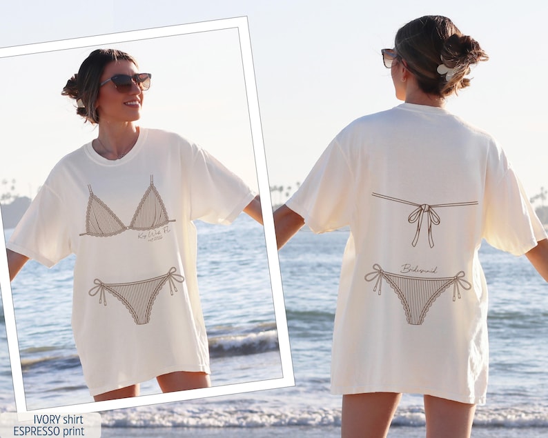 K&ouml;nnte beinhalten: Ein elfenbeinfarbenes T-Shirt mit einem espressofarbenen Grafikdruck. Die Vorderseite zeigt ein Bikini-Oberteil und -Unterteil mit dem Text "Ko We Fi". Die R&uuml;ckseite zeigt die Ansicht eines Bikinis mit dem Text "Bridesmaid" unter der Schleife.