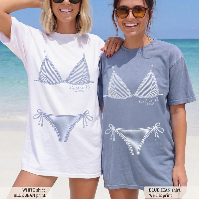 K&ouml;nnte beinhalten: Ein wei&szlig;es T-Shirt mit einem blauen Linien-Druck eines Bikinis und dem Text Key West, FL est 2026, sowie ein blaues T-Shirt mit einem wei&szlig;en Linien-Druck eines Bikinis und dem Text Key West, FL est 2026. Beide T-Shirts haben einen klassischen Rundhalsausschnitt.