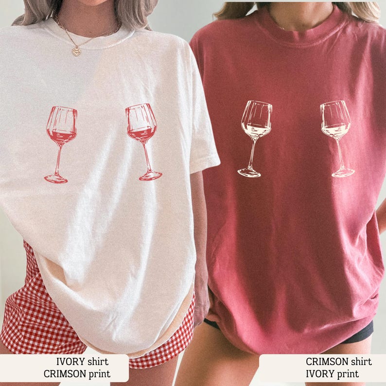 May include: Two t-shirts, one ivory and one crimson, each with a wine glass graphic. The ivory shirt has a crimson print, and the crimson shirt has an ivory print. The shirts are short-sleeved and have a casual style.