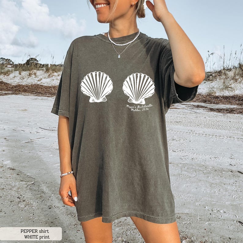 Puede incluir: Camiseta verde oliva oscuro con un dise&ntilde;o de concha blanca. La camiseta tiene el texto "Pepper's Bachelorette, Malibu, 2026". La camiseta es de corte holgado y se lleva en la playa.