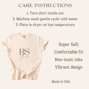K&ouml;nnte beinhalten: Ein cremefarbenes Kurzarm-T-Shirt mit einem quadratischen Logo mit der Aufschrift BS Studio. Der Text enth&auml;lt CARE INSTRUCTIONS: 1. Turn shirt inside out, 2. Machine wash gentle cycle: cold water, 3. Place in dryer on low temperature. Au&szlig;erdem aufgef&uuml;hrt: Super Soft, Comfortable fit, Non-toxic inks, Vibrant design und Made In USA.