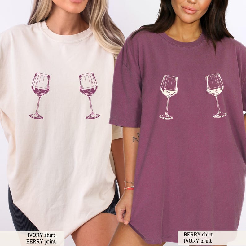May include: Two oversized t-shirts, one ivory and one berry, each featuring a wine glass graphic. The ivory shirt has a berry print, and the berry shirt also has an ivory print. The shirts are casual and comfortable, perfect for everyday wear.