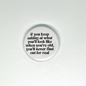 May include: A circular white pin-back button featuring black text that reads: if you keep asking ai what you'll look like when you're old, you'll never find out for real. The button has a smooth, glossy finish and a simple, clean design.