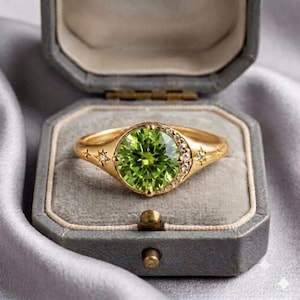 May include: A gold ring featuring a large, round, faceted lime green gemstone at the center. The band is decorated with small, engraved star motifs and a crescent-shaped accent set with tiny clear stones along the side of the main setting.