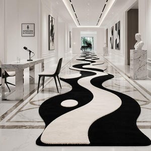 May include: A long, runner rug featuring a black and white wavy, yin-yang inspired pattern that stretches down a hallway. The rug has a soft, textured surface and is positioned on a polished white marble floor in a bright, modern interior space.