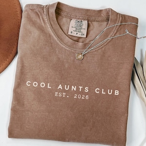 Minimalist Cool Aunts Club Est 2026 Comfort Colors shirt in dark neutral tone, modern aunt pregnancy announcement tee, trendy new aunt gift with clean typography aesthetic