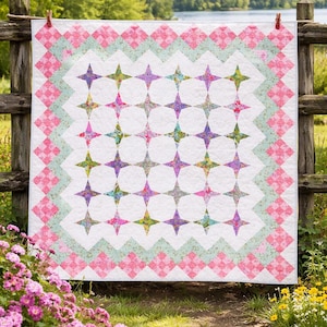 May include: A handmade quilt with a white background and a pattern of colorful star shapes. The quilt has a pink and green border with a diamond pattern. It is hanging on a wooden fence outdoors.