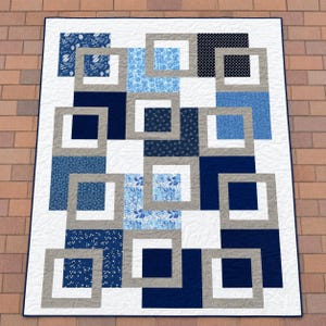 Peut inclure: Une courtepointe rectangulaire présentant un motif géométrique de carrés imbriqués dans des tons de bleu marine, bleu clair et gris. Le design inclut divers imprimés floraux et à pois sur un fond blanc avec une bordure bleu marine.
