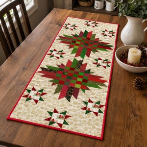 May include: A rectangular table runner featuring a cream-colored background with a mottled pattern. The runner displays two large central star motifs and several smaller star motifs in shades of red, dark green, and forest green, with a red border.