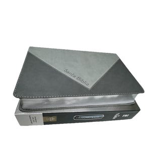 K&ouml;nnte beinhalten: Ein geschlossenes Buch mit grauem und schwarzem Einband. Der obere Einband ist grau mit einem schwarzen Dreieckmuster. Der Text "Santa Biblia" ist auf dem Einband aufgedruckt. Das Buch darunter tr&auml;gt den Text "THOMPSON" auf dem Buchr&uuml;cken.