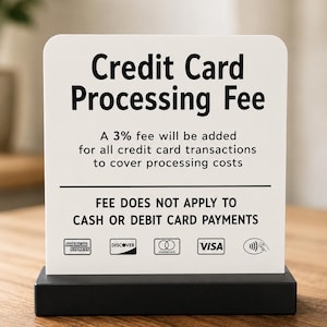 May include: A white rectangular sign with rounded top corners held in a black base. The text reads: Credit Card Processing Fee. A 3% fee will be added for all credit card transactions to cover processing costs. FEE DOES NOT APPLY TO CASH OR DEBIT CARD PAYMENTS. Logos for American Express, Discover, Mastercard, Visa, and a contactless payment symbol are at the bottom.
