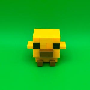 May include: A yellow, pixelated chick figurine with a brown beak and feet, and black eyes. The chick has small wings on either side of its body. The background is a solid green.