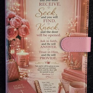 May include: A rectangular pink journal cover featuring a gold-toned graphic print of flowers, a candle, a crown, a Bible, and a pen. The text reads: Ask, and you shall RECEIVE. Seek, and you will FIND. Knock, and the door will be opened. Matthew 7:7.