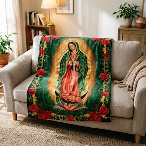 May include: A plush blanket featuring an image of Our Lady of Guadalupe. The blanket has a green background with red roses around the border. The central image depicts the Virgin Mary in a red and green robe, surrounded by a golden halo.