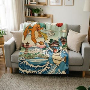 May include: A rectangular throw blanket featuring a colourful illustration of two creatures, one orange with wings and one blue with cannons, set against a landscape with a mountain, a pagoda, and ocean waves in a traditional woodblock print style.
