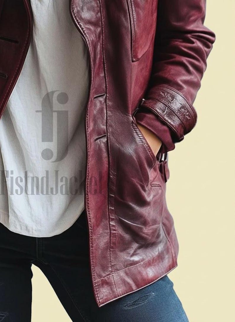 May include: A burgundy leather jacket with a button-up front and a pocket. The jacket has a classic design with a tailored fit. The sleeves have decorative detailing near the cuffs. The person is wearing a white shirt and blue jeans.