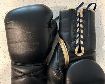 May include: A pair of black boxing gloves with gold trim and navy blue laces. The gloves have a stitched design and the letters "LY" are visible on one glove.