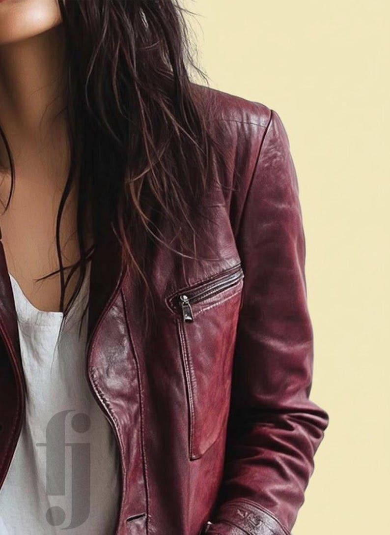 May include: A burgundy leather jacket with a zippered chest pocket and a silver zipper. The jacket is worn over a white top. The background is a solid light yellow.