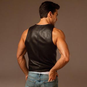 Pu&ograve; includere: Un gilet smanicato in pelle nera con finitura liscia e una cucitura verticale al centro della schiena. Il gilet &egrave; indossato sopra una maglietta bianca e abbinato a jeans in denim blu, presentando una silhouette aderente e un design pulito.