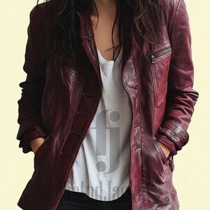 May include: A burgundy leather jacket with a button closure and a zippered chest pocket. The jacket has a classic design with a notched collar and a tailored fit. The model is wearing a white t-shirt and dark blue jeans.