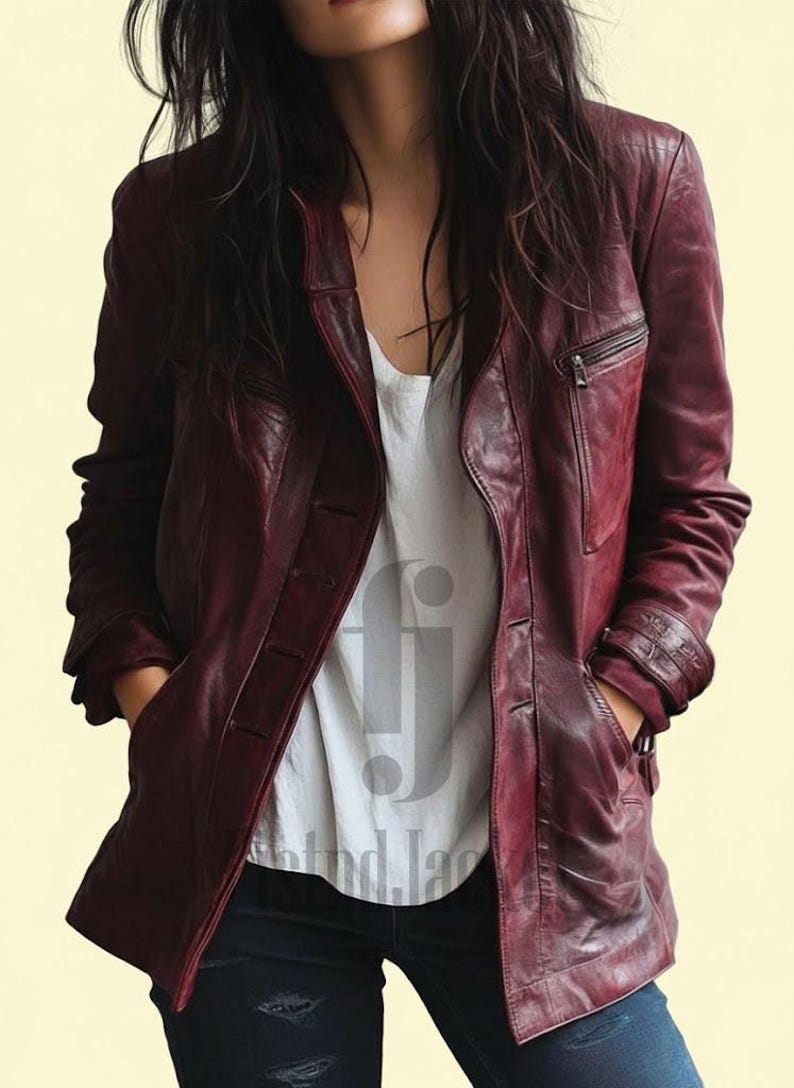 May include: A burgundy leather jacket with a button closure and a zippered chest pocket. The jacket has a classic design with a notched collar and a tailored fit. The model is wearing a white t-shirt and dark blue jeans.